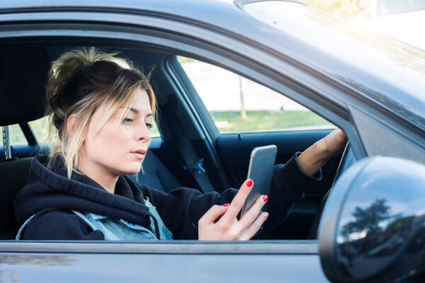 A teen girl driving while looking at her phone.