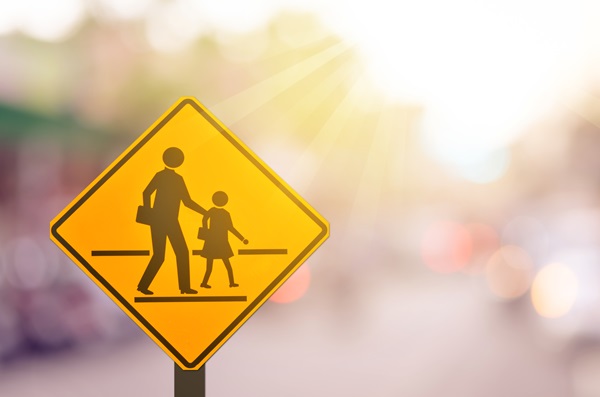 Yellow school zone sign with a blurred road and colorful light abstract background.