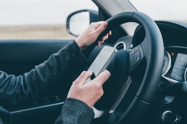 A driver operating a vehicle while holding a smartphone in one hand, a direct violation of Colorado’s hands-free law and a significant factor in local distracted driving accidents.